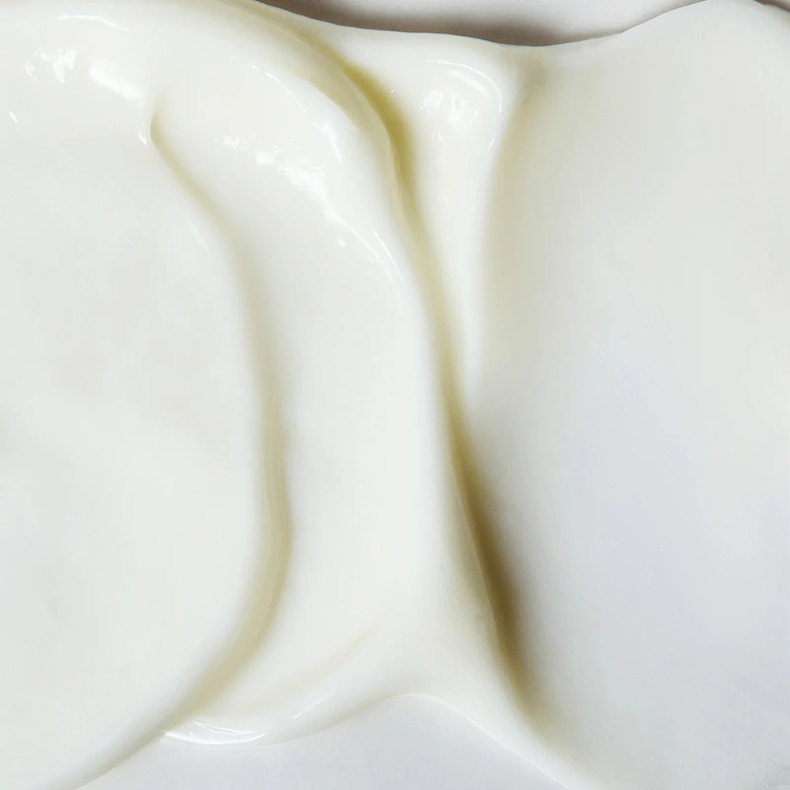 Close-up texture of smooth, creamy white moisturizer spread evenly on a flat surface with a glossy finish