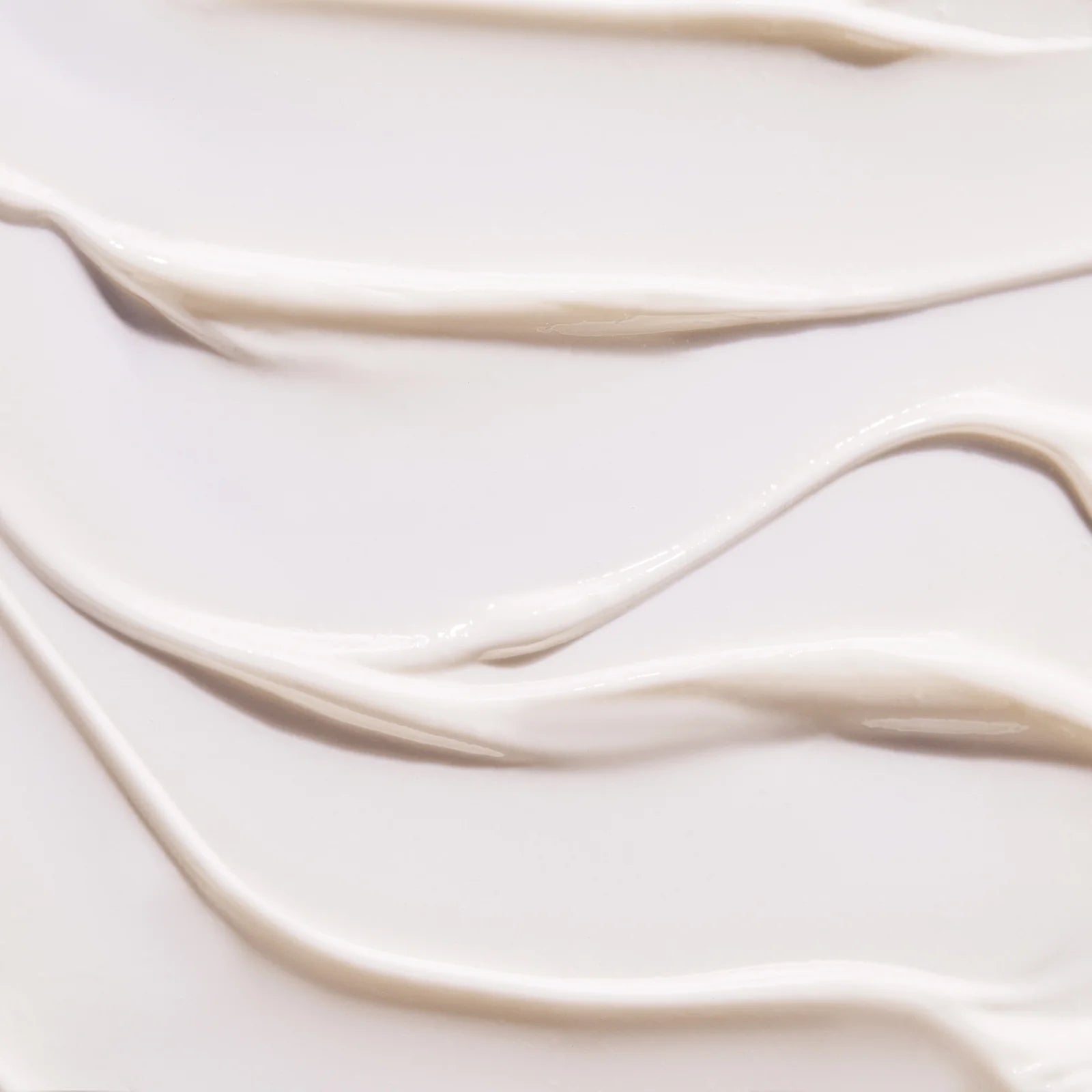 Close-up texture of smooth, creamy lotion or moisturizer spread in soft, wavy lines on a light surface.