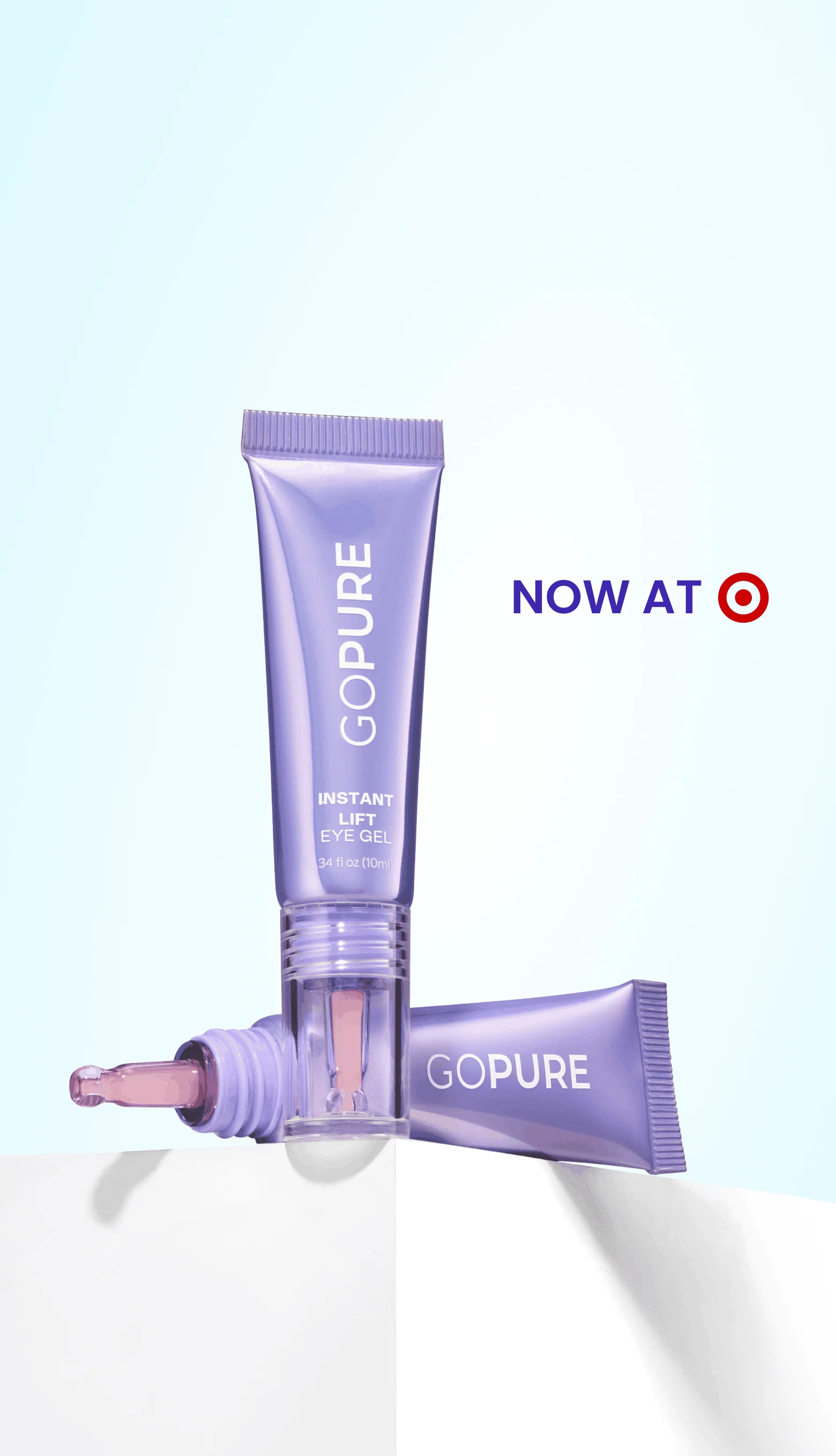 A purple tube of GO PURE Instant Lift Eye Gel is displayed against a light blue background. The tube is partially squeezed, revealing a dropper applicator with a pink tint. Beside it, another tube is positioned upright. The text "NOW AT Target" is featured prominently in the upper right corner, highlighting the product's availability. The overall composition showcases the eye gel's sleek design and emphasizes its eye care benefits.